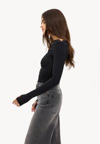 Zwarte bodysuit met lange mouwen, voorzien van een gerimpelde voorkant en een gestructureerd schouderdetail, gecombineerd met hoge taille grijze wijde jeans.