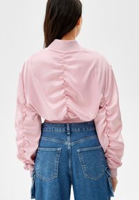 Rosa satängbombarjacka med samlade ärmar och ribbad nederkant, tillsammans med blå denimbyxor med hög midja som har stora bakfickor.