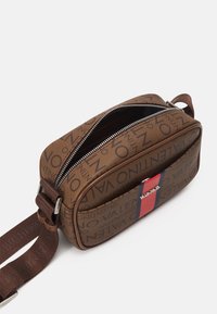 Brown rectangular crossbody bag with all-over Valentino logo print, front pocket with red and blue stripe detail, and a partially open zipper.