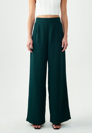 Wide-leg trousers in deep green fabric, high-waisted with pleat details, smooth texture, paired with a fitted white crop top.