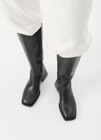 Μαύρες δερμάτινες μπότες μέχρι το γόνατο με τετράγωνη μύτη και μινιμαλιστικό σχέδιο, διαθέτοντας πλαινό φερμουάρ και χαμηλό, τετράγωνο τακούνι.