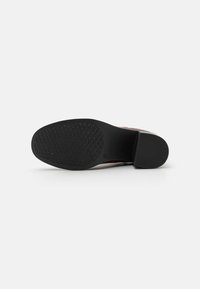 Suela de goma negra de un zapato con un agarre texturizado. La suela presenta un patrón en diamante y un tacón ligeramente elevado para mayor estabilidad.