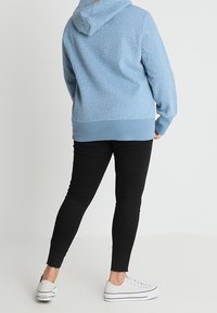 Persona con una sudadera ligera azul con puntos, jeans ajustados negros y zapatillas de plataforma blancas, de espaldas a la cámara.