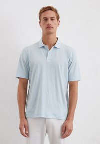 Lichtblauw polo-shirt van zachte stof, met een klassieke kraag, korte mouwen en een drieknoopsluiting. Minimalistisch ontwerp.