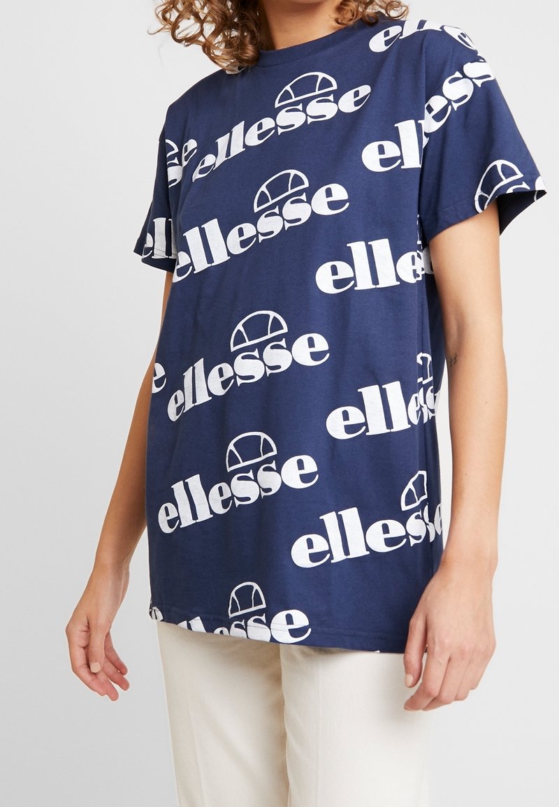 Navy blue cotton t-shirt featuring a repeated white "ellesse" logo and graphic design. Short sleeves, relaxed fit.