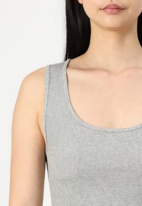 Harmaa ribbattu tank top, jossa on ympyräkaula-aukko ja leveät olkaimet, valmistettu pehmeästä, joustavasta kankaasta. Tasainen pinta ilman näkyviä kuvioita.