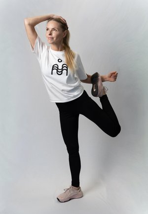 Valge särgiga ja mustades retuusides naine sirutab reielihast, hoides üht jalga selja taga, vaadates ülespoole.