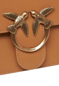 Tan leren handtas met een ronde bronzen hardware en twee vogelontwerpen, gegraveerde details en zichtbare stiksels langs de randen.