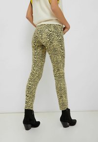 Gula och svarta randiga skinny jeans har hög midja, fem fickor och en figurnära design. De kombineras med svarta klackade ankelskortsstövlar.