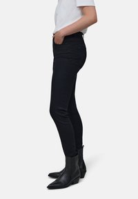 Jeans de mezclilla negros con corte Slim, cintura alta y bolsillos delanteros, combinados con botas de tobillo negras con punta afilada y diseño texturizado.
