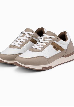 Paire de baskets casual beiges et blanches avec des lacets blancs et une doublure intérieure marron, présentée sur un fond blanc uni.