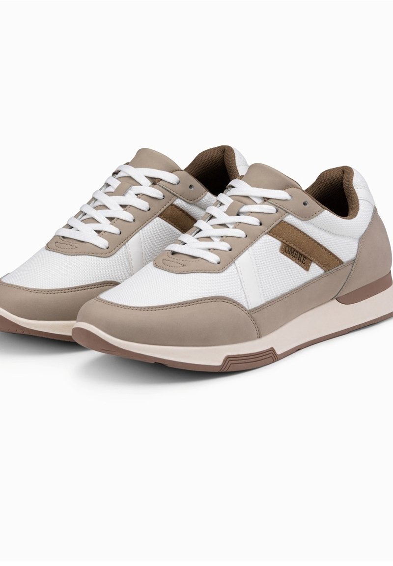 Paire de baskets casual beiges et blanches avec des lacets blancs et une doublure intérieure marron, présentée sur un fond blanc uni.