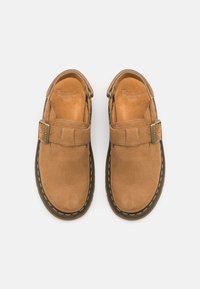Chaussures en cuir marron avec un design slip-on, un détail de boucle et des coutures jaunes le long de la semelle en caoutchouc noir. Texture lisse tout au long.