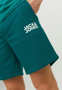 Teal cotton shorts featuring a white "JACK & JONES" logo on the left leg, with a classic design and smooth texture.