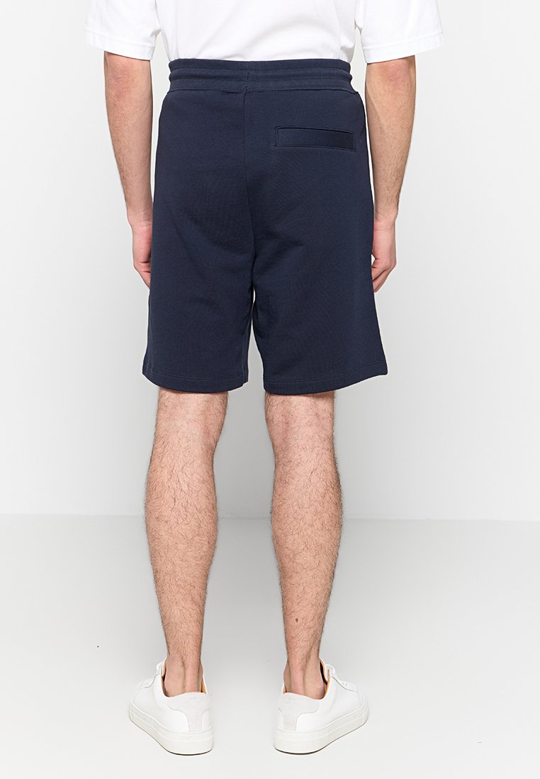 Mit einem elastischen Bund und einer Gesäßtasche ausgestattete navyblaue Baumwollshorts, die eine glatte Textur und eine lockere Passform bieten, kombiniert mit weißen Turnschuhen.