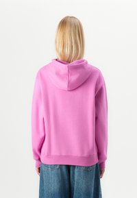 Różowa bluza z miękkiej tkaniny, z kapturem na sznurki i ściągaczami przy mankietach. Nosi się ją na dżinsowej spódnicy. Prosty i casualowy design.