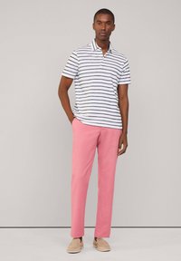 Polo shirt da uomo bianco con strisce navy, abbinato a pantaloni rosa. Presenta un colletto e maniche corte, creando un outfit casual.
