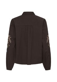 Blouse noire à manches longues vue de dos, avec une broderie florale sur les deux manches et un détail de tissu froncé sous l’empiècement.