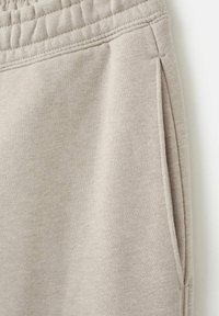 Beige Jogginghose aus strukturiertem Stoff, mit elastischem Bund und seitlichen Taschen, in Nahaufnahme dargestellt.