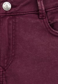 Burgundska traperica s glatkom teksturom, koja ima vidljive šavove, prednji džep i srebrnu dugmad s logotipom "Blue Ridge".