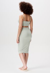 Hellgrünes, geripptes Zweiteiler-Outfit mit einem taillierten Crop-Top mit verstellbaren Trägern und einem knielangen Rock. Glatte Textur; minimalistisches Design.