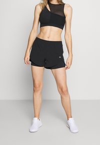 Svart sport-bh med meshpaneler och åtsittande shorts med en lätt flare. Vita sneakers fulländar den sportiga looken.