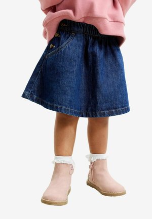 Denim seeliku flare-disainiga, tumedast sinisest kangast, elastse vöökohaga, millel on nööpide aktsendid. Kombineeritud heledate roosa värvi pahkluu saapade ja valgete volangiliste sokkidega.