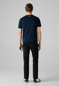 Marineblauwe t-shirt met korte mouwen en een ronde halslijn. De achterkant heeft een klein wit logo. Gecombineerd met zwarte jeans en casual schoenen.