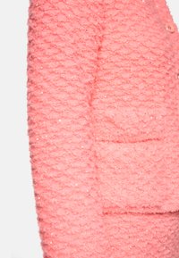 Rosa strukturierte Jacke mit gemustertem Gewebe und Pailletten, sichtbaren Knöpfen und einer aufgesetzten Tasche an der Seite.