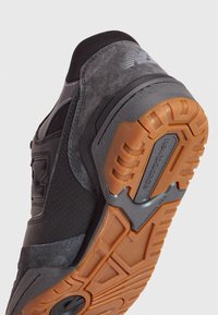 Svart mocka och mesh sneakersula, med en orange icke-märker gummi botten som har texturerade greppmönster och varumärkesdetaljer.