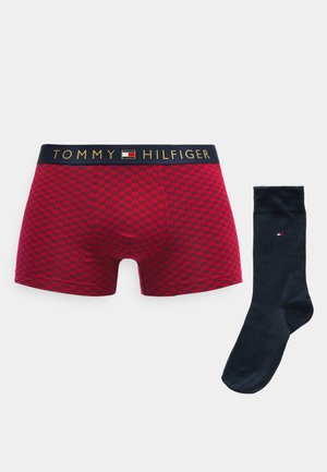 Red boxer shorts with a checkered pattern and a navy waistband featuring the "TOMMY HILFIGER" logo, paired with a plain navy sock.