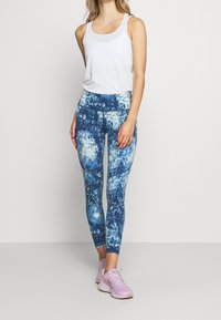 Leggings blu e bianchi macchiati con vita alta, abbinati a un top bianco e scarpe da ginnastica rosa chiaro, tutto aderente.