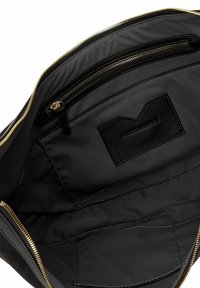 Interno di una borsa in tessuto nero con una texture liscia, dotata di una tasca con zip e di un'etichetta in pelle. Visibile l'hardware della zip dorata.
