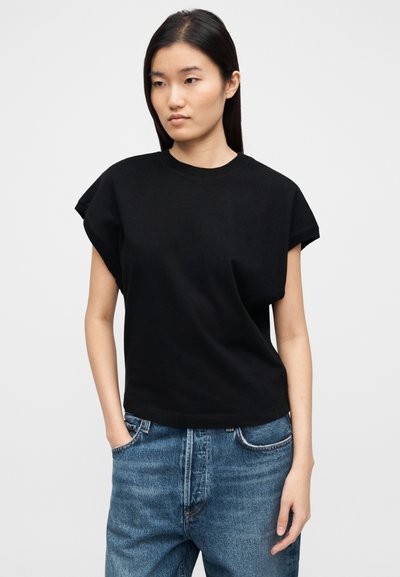 Schwarzes T-Shirt mit kurzen Ärmeln aus Baumwolle, mit Rundhalsausschnitt, legerer Passform und umgeschlagenen Bündchen, kombiniert mit blauen, hoch taillierten Jeans.