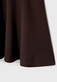 Ourlet de jupe en tissu marron foncé avec des coutures visibles sur un fond gris clair.