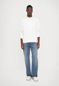 Sudadera blanca de cuello redondo, combinada con jeans rectos de un azul claro. El atuendo se complementa con zapatillas blancas.