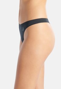 Zwarte string ondergoed met een naadloos ontwerp, gemaakt van zachte stof, met een dunne tailleband en een subtiel logo aan de zijkant.