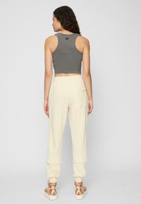 Grijze cropped tanktop gecombineerd met crèmekleurige joggingbroek met een elastische tailleband, omgeslagen mouwen en sneakers met een tan ontwerp.