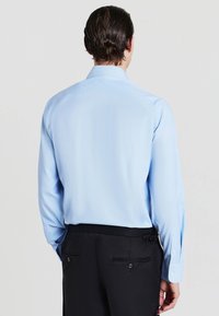 Camicia azzurra a maniche lunghe con colletto a punta, texture liscia, polsini con bottone e design della schiena dritta, abbinata a pantaloni neri.