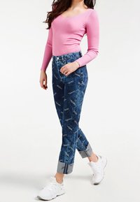 Różowy prążkowany top z długim rękawem, zestawiony z niebieskimi dżinsami z nadrukiem i podwiniętymi mankietami; białe trampki dopełniają stylizację.