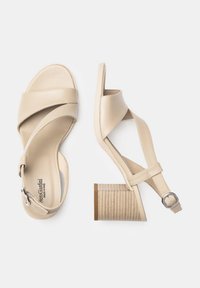 Sandalias de cuero beige con punta abierta y diseño de tira cruzada, y un tacón bloque texturizado. Cuentan con una correa en el tobillo con hebilla ajustable.