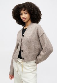 Kavos megztinis su V formos iškirpte, raišteliu apatinėje dalyje ir keturiais mygtukais. Nešiojamas ant juodos laisvos formos marškinėlių. Minkšta tekstūra.