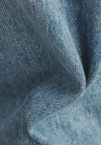 Denimstof in verschillende tinten blauw, met een gestructureerd oppervlak en een keperpatroon, licht gekreukt voor visuele diepte.
