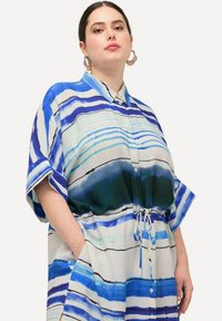 Vestido camisero a rayas en tonos azules y verdes, con mangas cortas, cierre de botones en el frente, cintura ajustable con cordón y bolsillos laterales. Tela suave y ligera.
