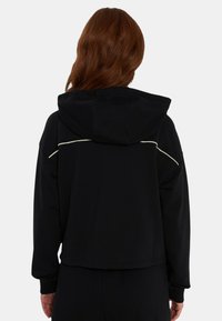 Felpa nera corta in tessuto morbido con cappuccio con coulisse, piping bianco a contrasto sul retro e polsini a costine.