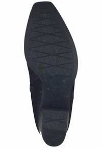 Semelle en caoutchouc noir avec un motif de bande de roulement texturé, présentant des bords lisses et un léger talon. Détails comprenant le nom de la marque embossé.