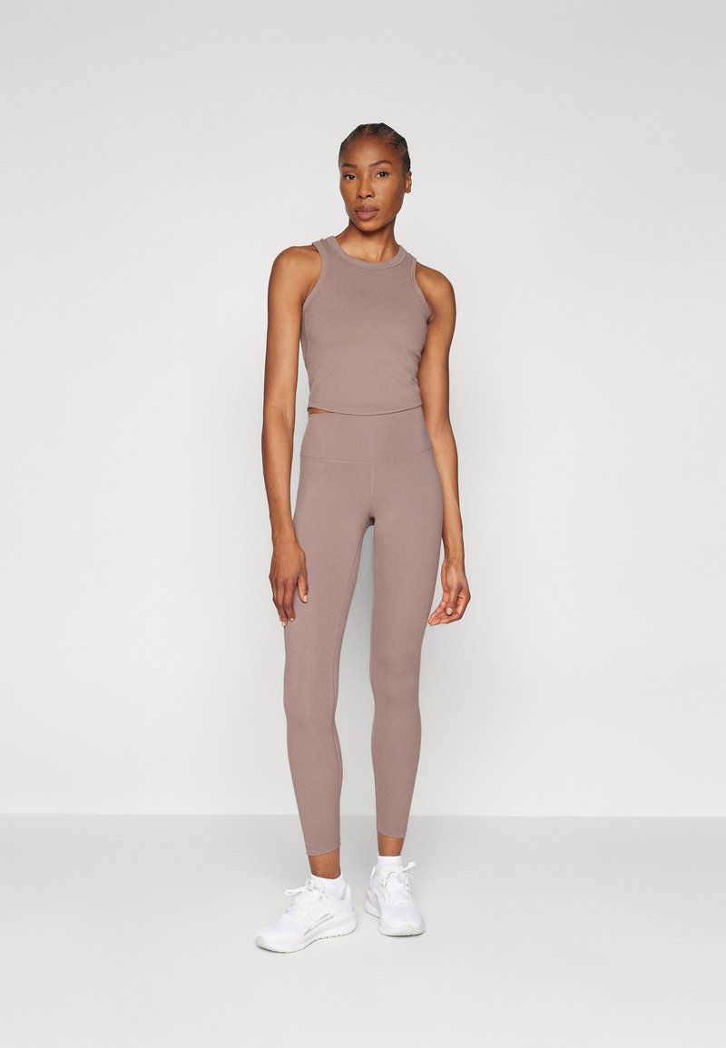 Lichtbruine sporttanktop en leggings gemaakt van rekbare stof, gecombineerd met witte sportschoenen. Slim fit ontwerp met een gladde textuur.