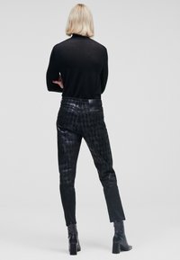 Svart långärmad topp i kombination med svarta mönstrade smala byxor. Byxorna har en glänsande yta och en något sliten look. Svarta klackstövlar.