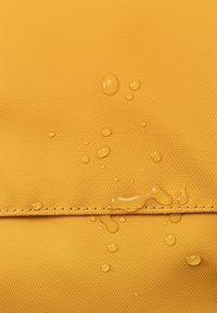Tessuto giallo resistente all'acqua con una superficie texturizzata, con gocce sopra e una cucitura come dettaglio notevole.