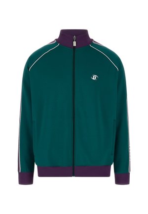 Chaqueta verde con cremallera y cuello alto, rayas blancas en las mangas y puños de color púrpura con canalé. Presenta un logotipo en el pecho.